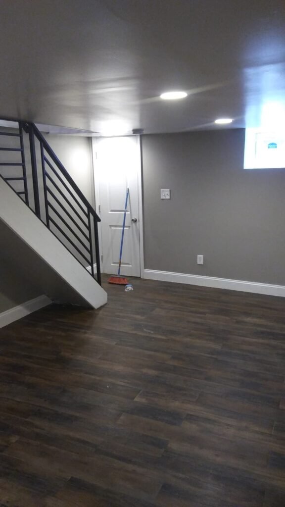Finished lower level with dark vinyl plank flooring, recessed lights, a metal stair railing and gray walls