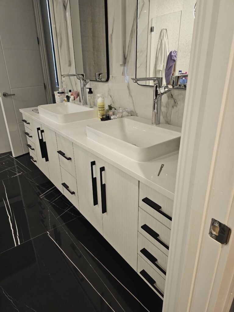 Remodeled bathroom with a double vanity, white cabinets with black pulls, vessel sinks and dark floor tile
